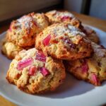A close-up of several Amazing Rhubarb Cookies piled on a white plate, dusted with powdered sugar and studded with bright pink rhubarb pieces.