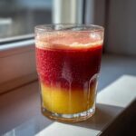Close-up of a glass containing layered Apple Cranberry Ginger Lemon Detox Juice, showing a bright yellow bottom layer and a deep red top layer.