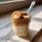A delicious jar of Banana Peanut Butter Overnight Oats topped with fresh banana slices and peanut butter.