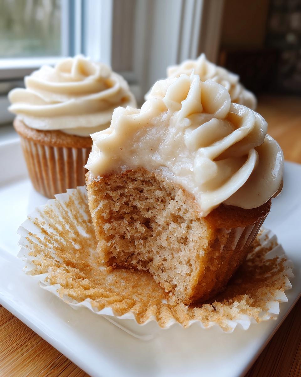 Close-up of The Best Banana Cupcakes Maple Buttercream, showing a bite taken out to reveal the moist crumb and thick frosting.