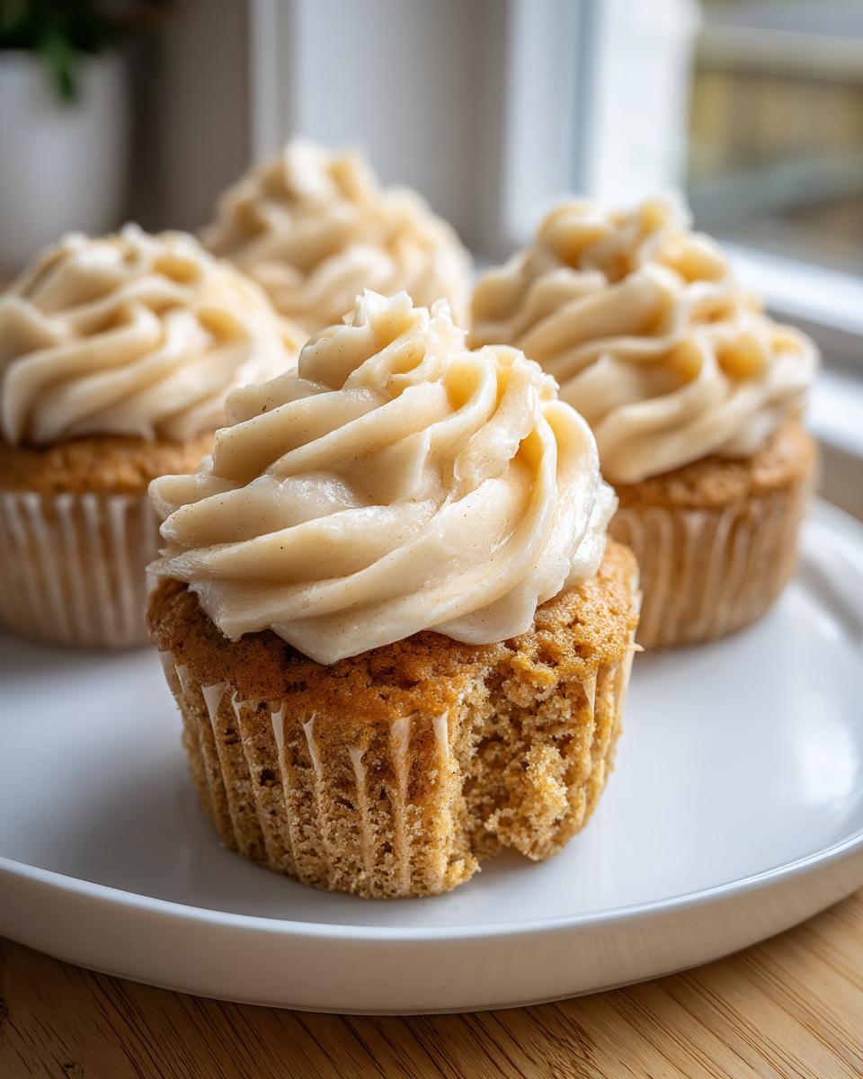 A close-up of one of The Best Banana Cupcakes Maple Buttercream with a bite taken out, showing moist cake and thick frosting.
