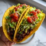 Two crispy hard-shell Best Summer Vegan Tacos filled with black beans, lettuce, and topped with salsa.