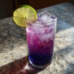 Close-up of a tall glass filled with a vibrant purple Blueberry Ginger Lime New Years Mocktail, garnished with a lime wheel.