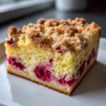Close-up of a moist slice of Breakfast Lemon Raspberry Coffee Cake featuring bright red raspberries and a crumbly streusel topping.