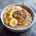 A close-up of a bowl of Breakfast Peanut Butter Banana Chia Oats, topped with sliced bananas and a drizzle of honey.