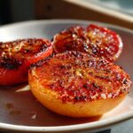 Close-up of broiled maple cinnamon grapefruit strawberries, caramelized and slightly charred, on a white plate.