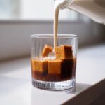 Milk being poured over frozen Caramel Coffee Ice Cubes Latte cubes in a glass.