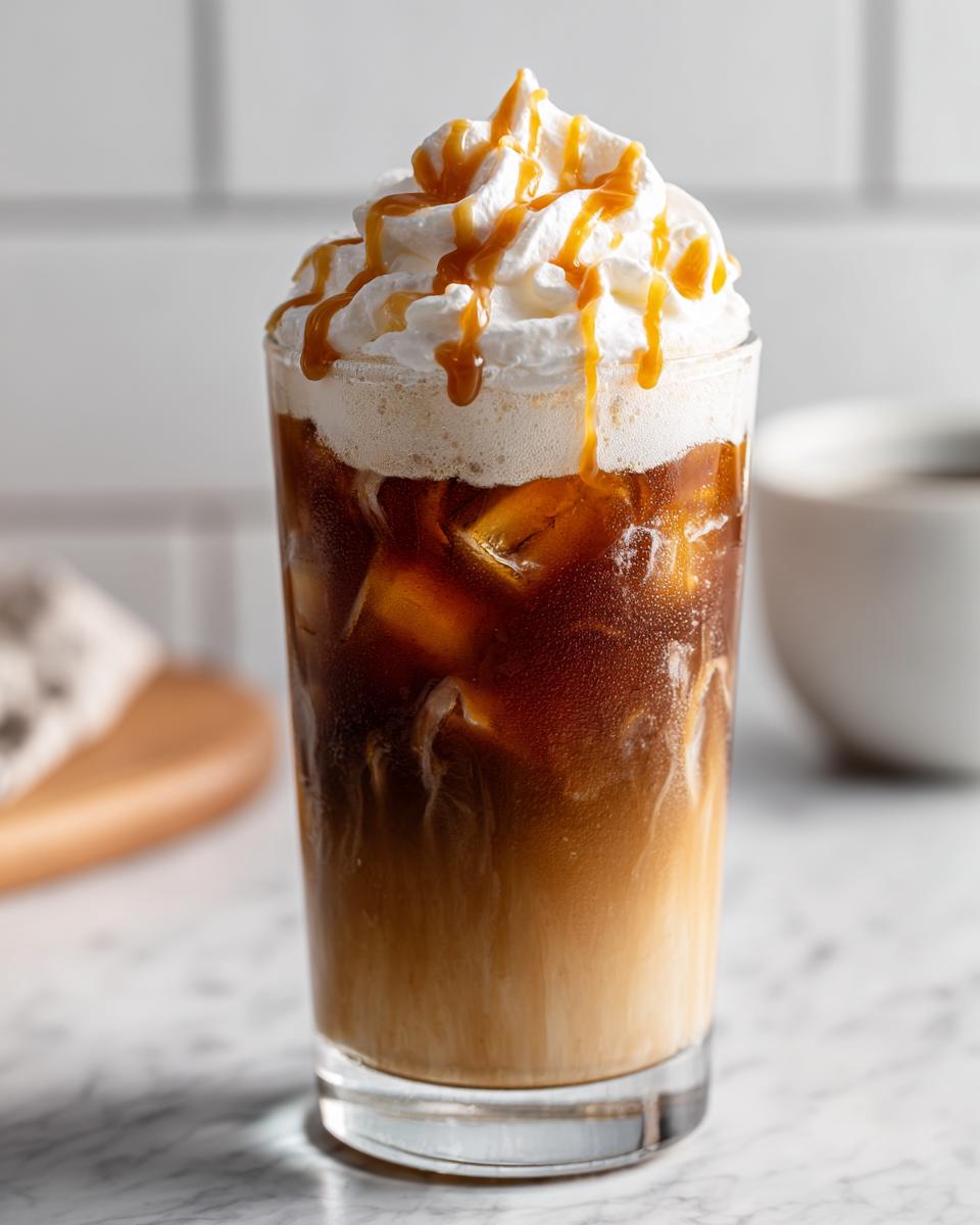 A refreshing Caramel Oat Latte Mocktail topped with whipped cream and caramel drizzle, served over ice.