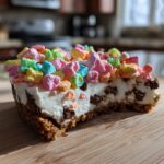 A slice of Chocolate Chip Cheesecake Lucky Charms on a wooden board, topped with colorful marshmallows.