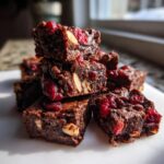 A stack of rich, fudgy Chocolate Cranberry Almond Snack Bars studded with bright red cranberries and whole almonds.