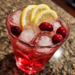 A refreshing Cranberry Lemonade Ice Cube Spritzer with fresh cranberries and lemon slices in a glass filled with ice.