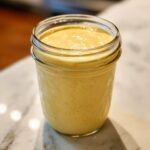 A glass jar filled with creamy lemon garlic dressing dairy free, showing its smooth texture and pale yellow color.