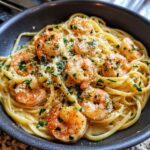 A close-up of a skillet filled with creamy shrimp scampi pasta, topped with fresh parsley and grated cheese.