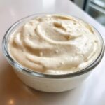 Close-up of thick, creamy Vegan Ranch Dressing swirled in a clear glass bowl.