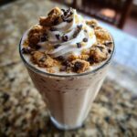 A tall glass of Dairy Free Chocolate Chip Cookie Milkshake topped with whipped cream, cookie crumbles, and chocolate chips.