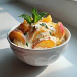 A white bowl filled with Delightful Peaches and Cream, topped with fresh mint leaves.