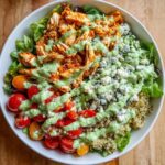 A vibrant Easy Green Goddess Buffalo Chicken Bowl overflowing with shredded buffalo chicken, cherry tomatoes, blue cheese, quinoa, and lettuce, drizzled with green goddess dressing.