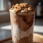 Close-up of an Easy Peanut Butter Chunky Monkey Milkshake with chocolate swirls, topped with caramel drizzle and chopped peanuts.