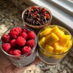 Three glasses of healthy chia pudding topped with raspberries, mango chunks, and goji berries.