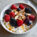 A close-up of a Healthy Greek Yogurt Breakfast Bowl topped with mixed berries, almonds, and honey.