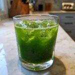 A close-up of a glass filled with vibrant green Healthy Kale Lemonade and ice, showing condensation on the glass.