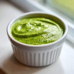 A close-up of thick, bright green Homemade Green Goddess Dressing served in a small white fluted ramekin.