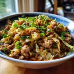 Close-up of a bowl filled with Irresistible Egg Roll In A Bowl, featuring ground meat, cabbage, and green onions.
