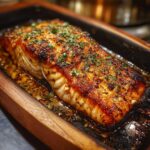 Close-up of a perfectly cooked, flaky Irresistible Garlic Butter Salmon fillet in a rustic wooden dish, glistening with butter and herbs.