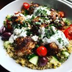 A close-up of Irresistible Greek Chicken Bowls featuring seasoned chicken, quinoa, cucumber, tomatoes, olives, feta, and tzatziki sauce.