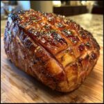 Close-up of a perfectly glazed ham, glistening with an irresistible ham glaze, scored and garnished with herbs.