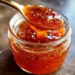 A spoonful of Irresistible Honey BBQ Sauce Recipe being lifted from a glass jar.