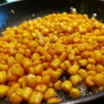 Close-up of Irresistible Honey Butter Skillet Corn cooking in a black skillet, glistening with butter.