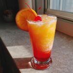 A refreshing Jamaican Me Happy Mocktail layered with orange and red juices, garnished with an orange slice and cherry.