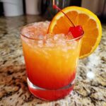 A vibrant Jamaican Rum Punch Mocktail served over ice, garnished with an orange slice and maraschino cherry.