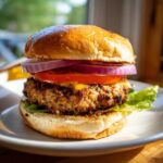 Close-up of a fully assembled Jerk Turkey Burger with melted cheese, red onion, tomato, and lettuce on a brioche bun.