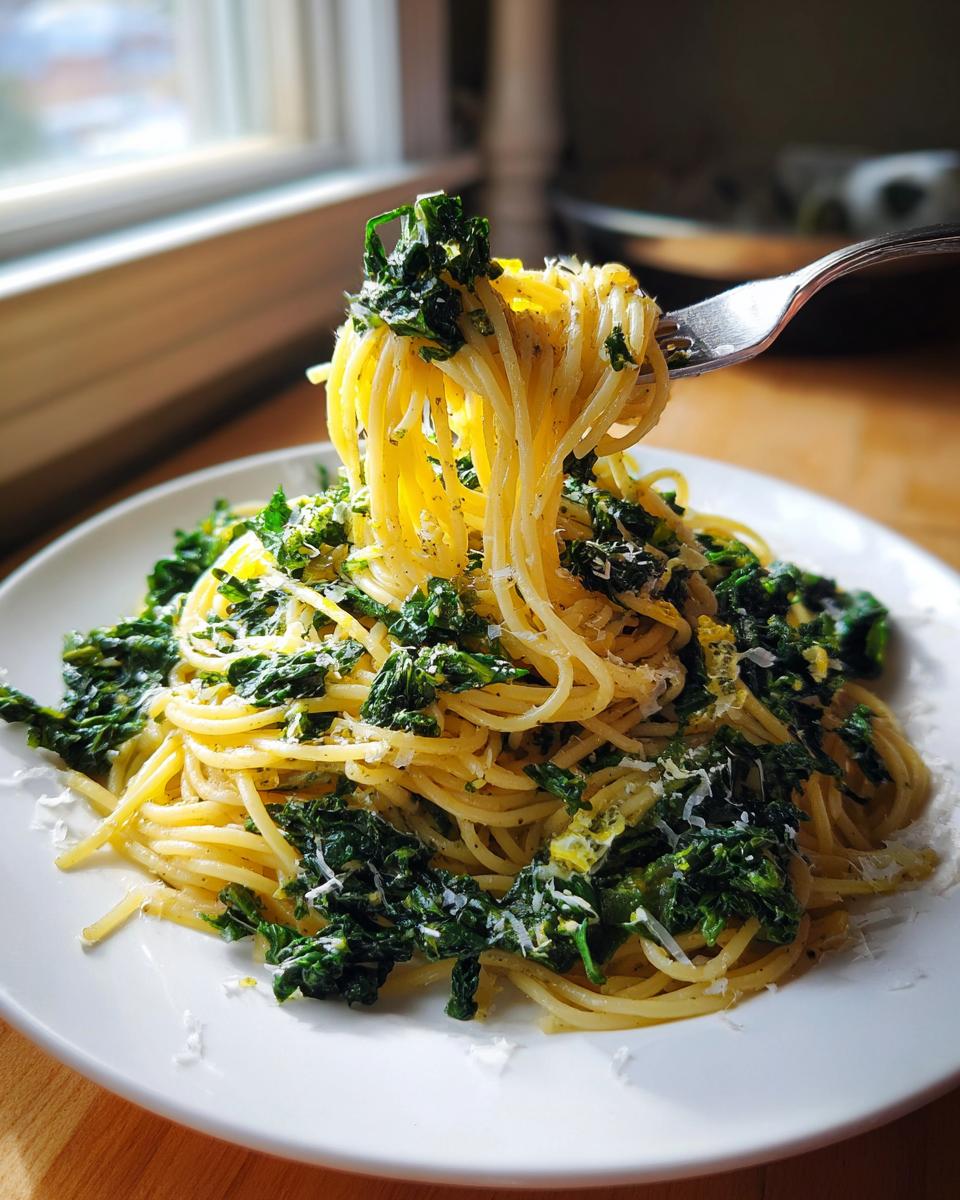 A fork lifting a swirl of Lemon Herb Garlic Parmesan Kale Pasta from a white plate.