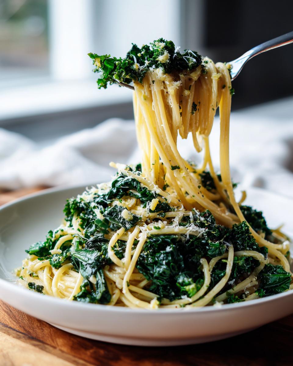 A fork lifting strands of Lemon Herb Garlic Parmesan Kale Pasta topped with shredded cheese.