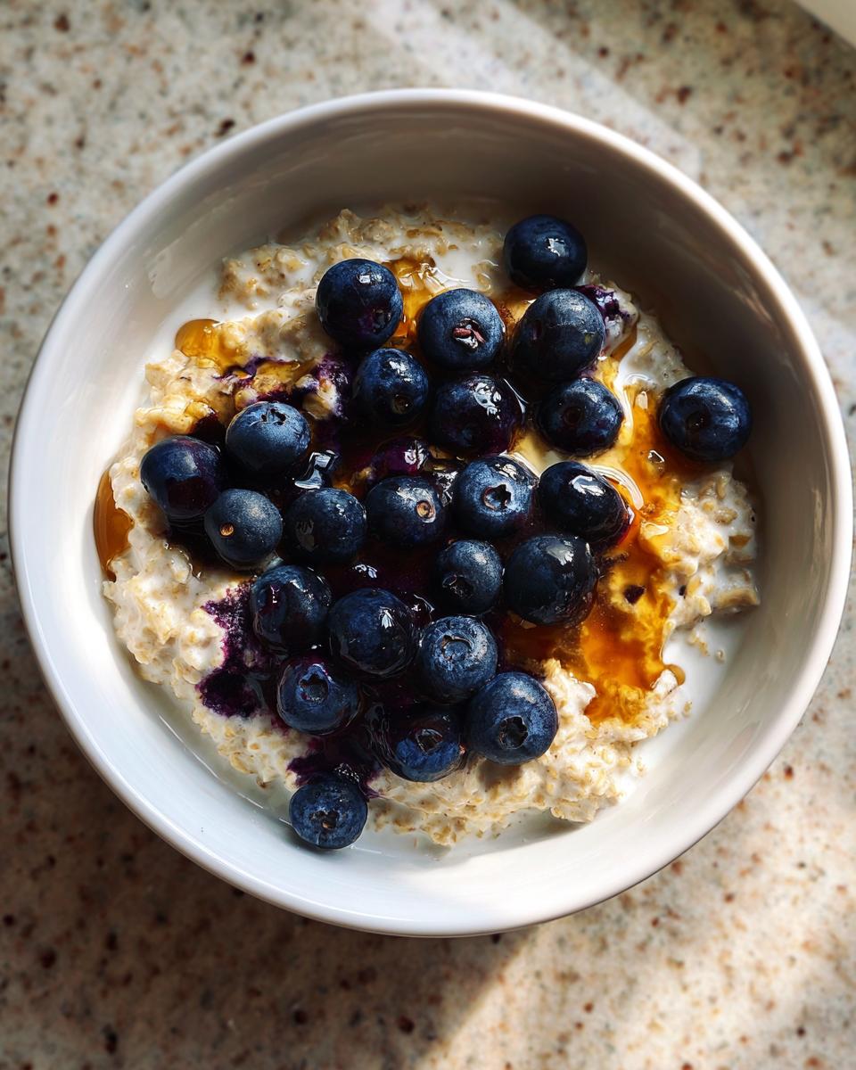 A close-up overhead view of a bowl of Maple Blueberry Oatmeal Porridge, topped with fresh blueberries and drizzled with syrup.