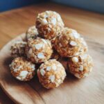 A stack of no bake white chocolate energy bites coated in chopped almonds on a wooden board.