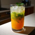 Close-up of a vibrant Orange Kiwi Ginger Mocktail layered with crushed ice and mint garnish.