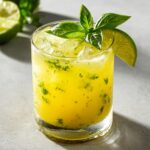 A close-up of a Pineapple Coconut Basil Mocktail With Lime, garnished with fresh basil and a lime wedge.