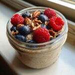 Close-up of Protein Overnight Quinoa in a jar, topped generously with fresh raspberries, blueberries, and chopped pecans.