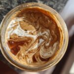 Overhead view of Protein Peanut Butter Jelly Overnight Oats in a jar, with swirls of cream and peanut butter.