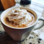 A close-up of a Salted Caramel Cashew Latte topped with whipped cream and a sprinkle of cinnamon.
