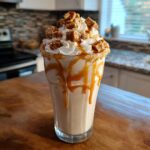 A tall glass filled with a creamy Salted Caramel Chunky Milkshake, topped with whipped cream, caramel drizzle, and chunks of candy.