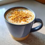 A close-up of a Toasted Coconut Honey Latte in a blue mug, topped with toasted coconut flakes.