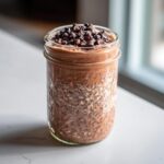 A glass jar filled with Triple Chocolate Protein Overnight Oats, topped with chocolate chips.