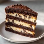 Close-up of a decadent slice of Vegan Brownie Cookie Dough Cake showing multiple layers of dark chocolate cake and creamy filling with chocolate chips.