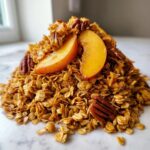A mound of Vegan Caramelized Peach Cinnamon Granola topped with caramelized peach slices and pecans.