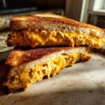 A delicious vegan chickpea tuna melt sandwich, cut in half, with melted vegan cheese oozing out.